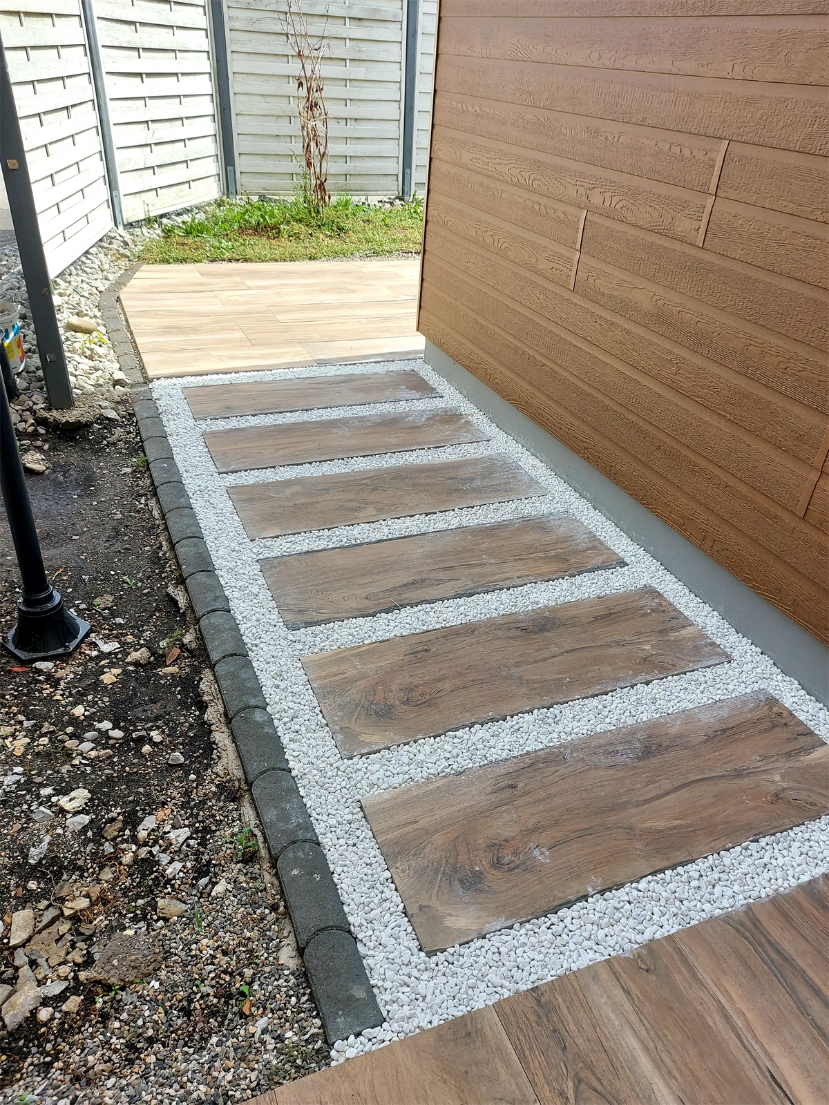 Détail d’un cheminement en dalles aspect bois séparées par du gravier blanc