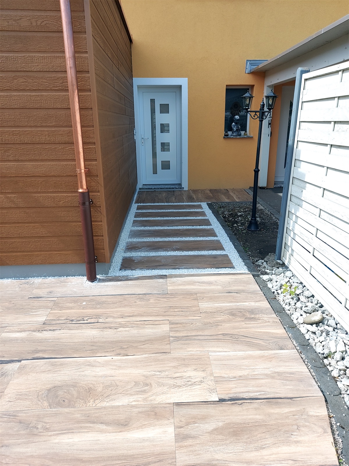 Entrée de maison aménagée avec dalles aspect bois, gravier blanc et bordures