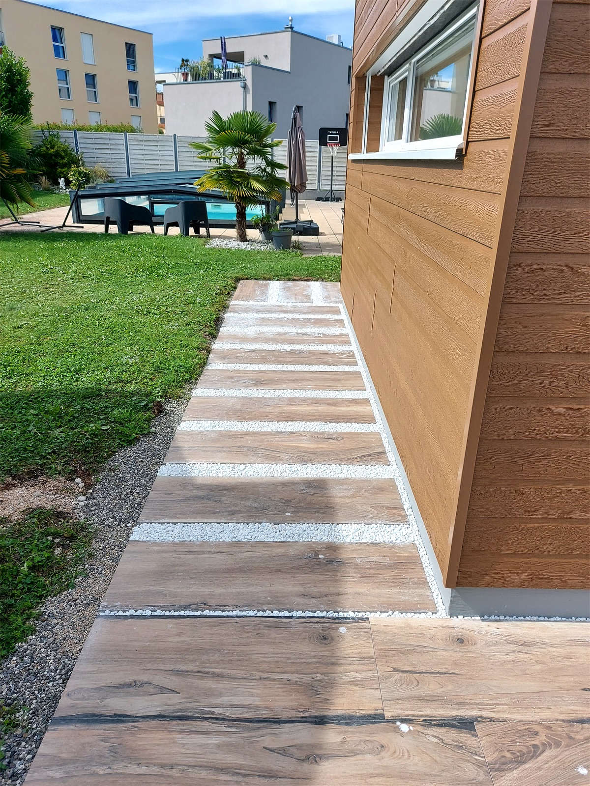 Allée extérieure en dalles aspect bois et gravier blanc longeant une maison