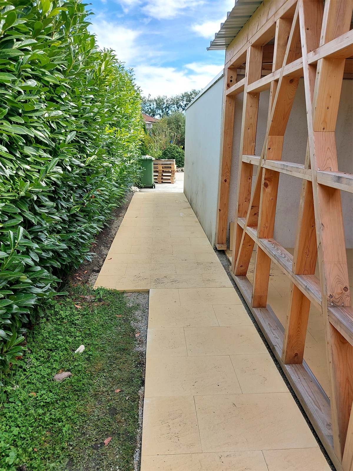 Passage en dalles longeant une haie et une ossature bois en cours de construction